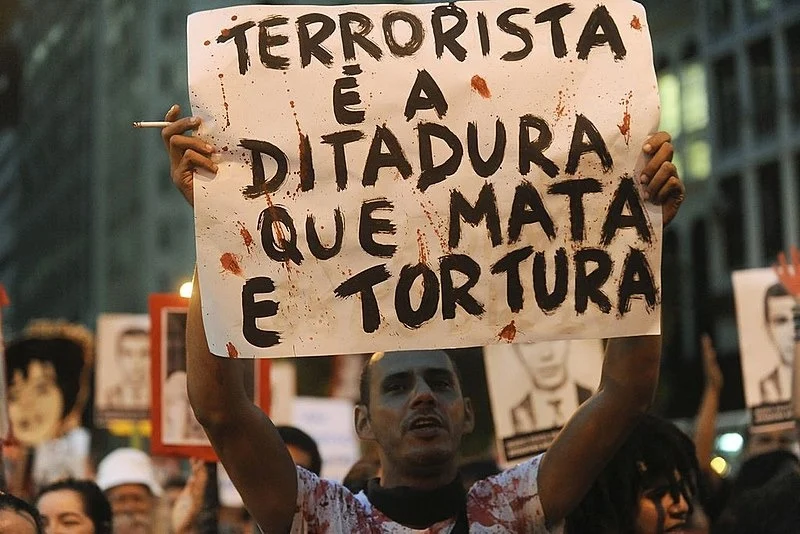 Homem segura um cartaz onde sê lê: Terrorista é a ditadura que mata e tortura
