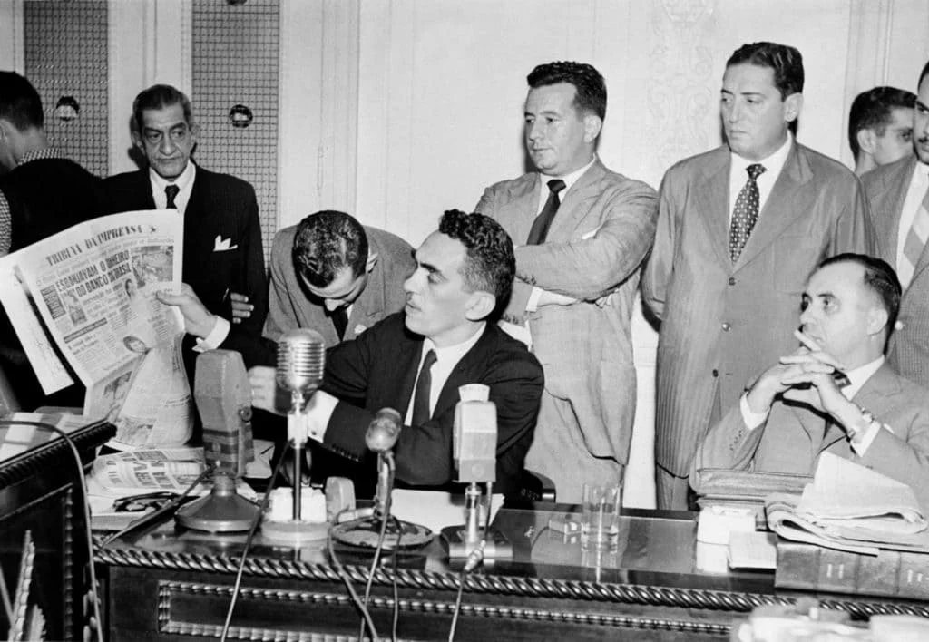 CPI da Última Hora Samuel Wainer, ao centro e segurando um exemplar de jornal, defende-se perante os integrantes da chamada “CPI da Última Hora”, durante sessão realizada em julho de 1953. Imagem: Arquivo Nacional