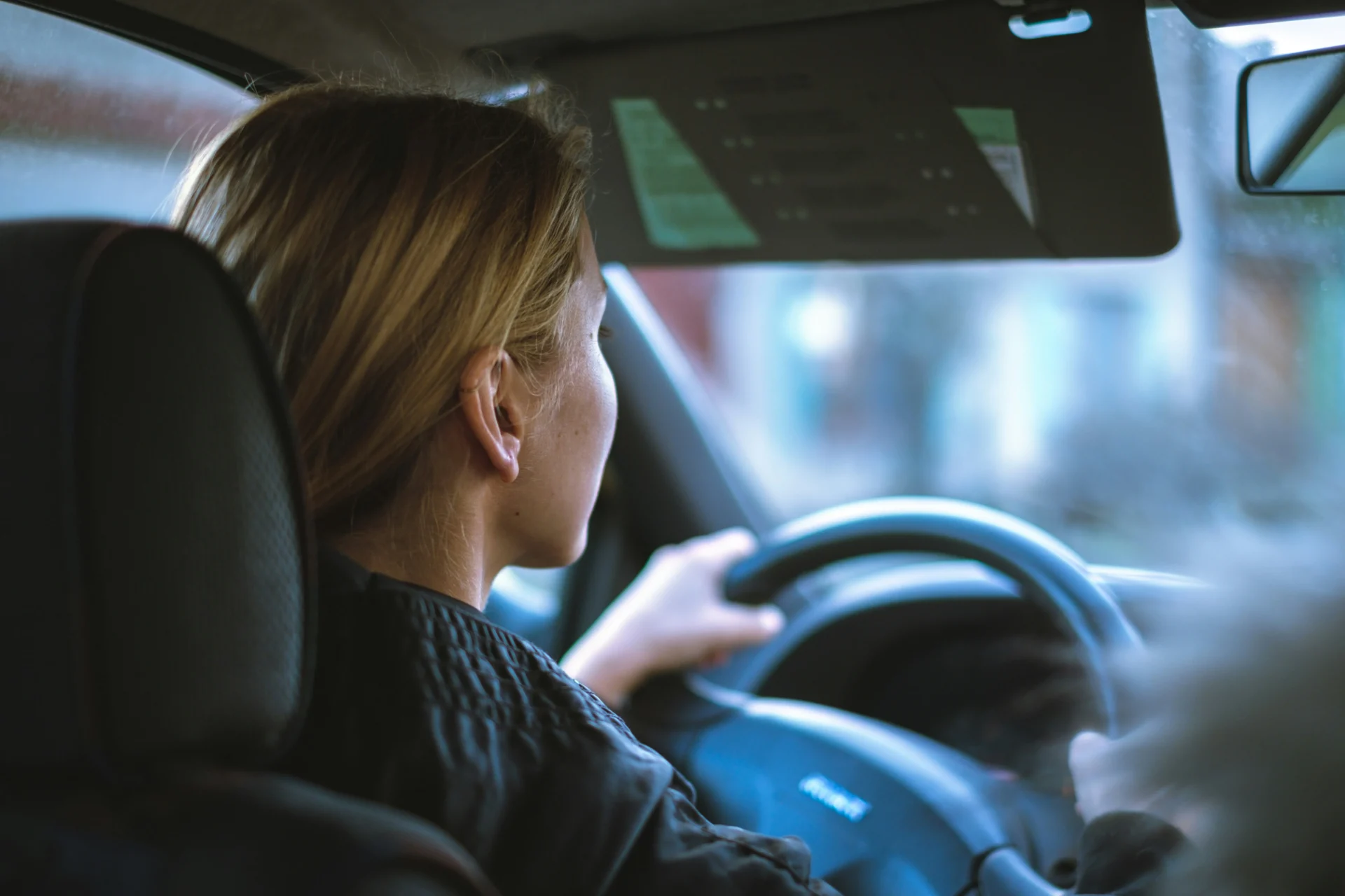 Mulher loira de perfil dirigindo carro, com uma mão no volante