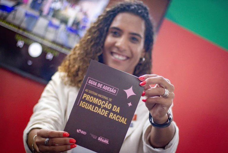 Na foto, a ministra da Igualdade Racial, Anielle Franco, segura o novo Guia de Adesão ao Sistema Nacional de Promoção da Igualdade Racial (Sinapir), lançado em junho de 2023 pelo ministério como parte da atualização das diretrizes de cooperação entre estados, municípios e a União no enfrentamento ao racismo. Imagem: reprodução 