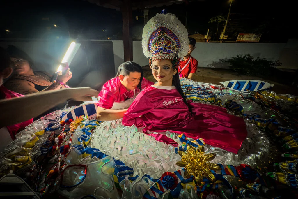 Guilherme Borari, coordenador de itens, finaliza a preparação da Rainha do Sairé, Maria Eulalia, na entrada da Arena dos Botos. Para ele, o calor crescente exigiu a criação de indumentárias mais leves e resistentes, mesmo à noite (Foto: Leonardo Milano/Repórter Brasil)