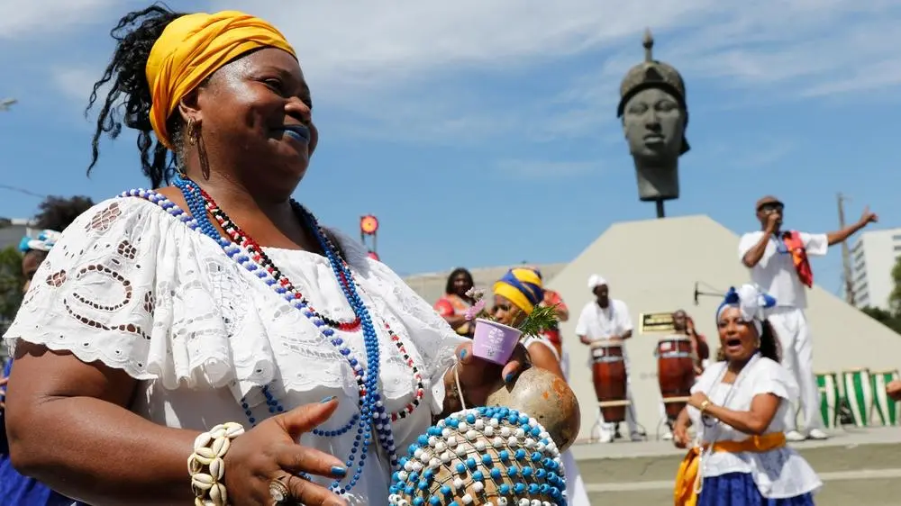 Cultura afro brasileira Mulher afro-brasileira usando colares, tranças, búzios e tocando música. Imagem: reprodução