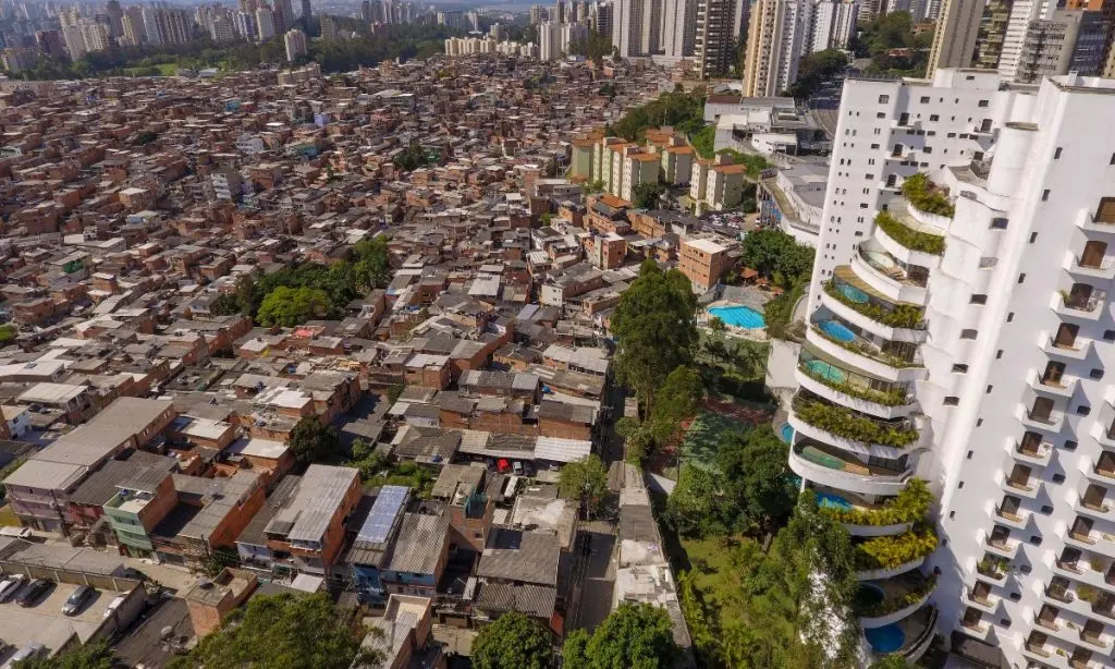 De um lado, piscina na varanda; do outro, moradias precarizadas. A imagem escancara a desigualdade social que a meritocracia insiste em chamar de “mérito”. Imagem: iStock