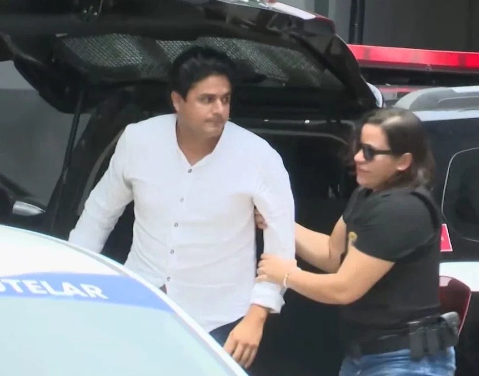 O cantor João Lima sendo conduzido à delegacia por uma policial feminina