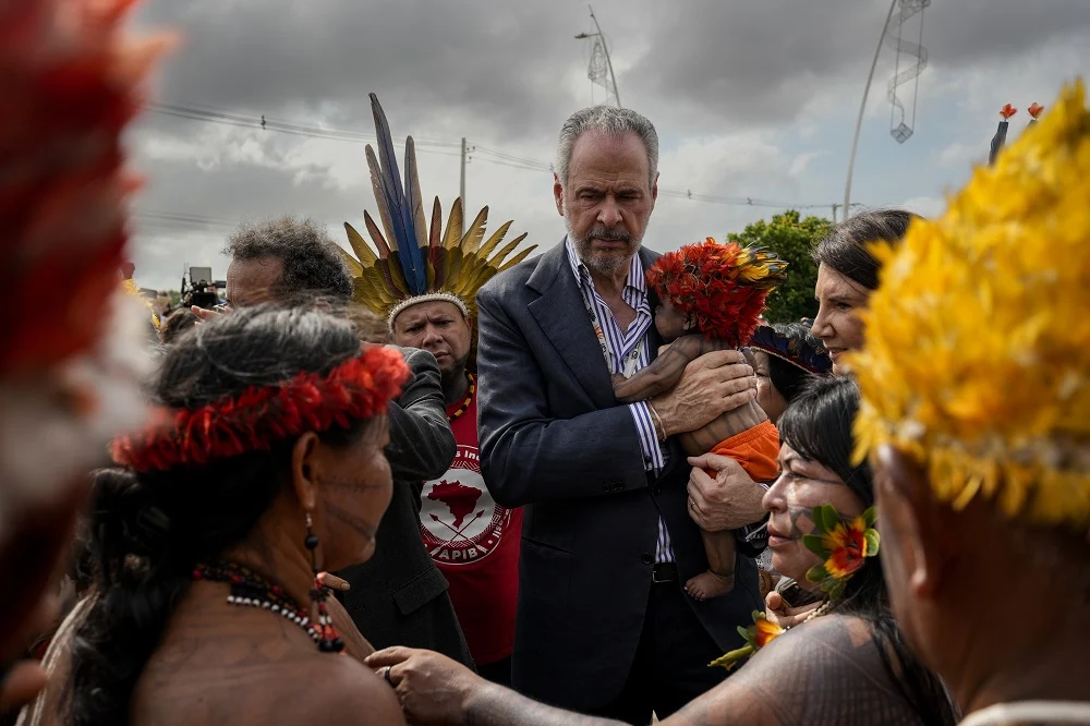 O embaixador André Corrêa do Lago, presidente da COP30, segura o filho da ativista Maria Leusa Munduruku durante as negociações para liberar a entrada da Blue Zone. Ao lado dele está Ana Toni (de perfil), CEO da COP30, e à frente dele aparece a ativista Alessandra Munduruku (Foto: Fernando Martinho/Repórter Brasil)