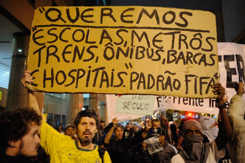 Manifestante segura cartaz pedindo equipamentos públicos no "padrão FIFA", em alusão grandes investimentos realizados em obras de infraestrutura para a Copa do Mundo de 2014. Foto: Wikimedia Commons 