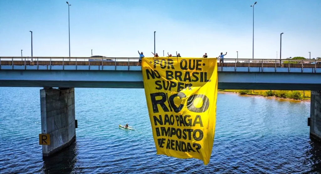 Manifestantes estendem faixa na Ponte Juscelino Kubitschek exigindo a taxação dos super ricos no Brasil.