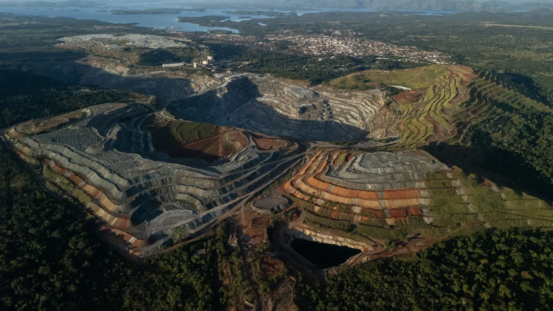 Vista aérea panorâmica de uma vasta mina a céu aberto em Minaçu, Goiás, com escavações em degraus e áreas de mata nativa ao redor. Ilustra as reservas estratégicas de minerais essenciais para a transição energética.