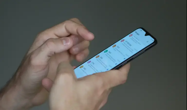 Mãos seguram um smartphone com a tela iluminada exibindo notificações em aplicativos. A imagem contextualiza o papel das plataformas digitais na amplificação do pânico moral e das fake news: algoritmos que priorizam o engajamento favorecem a circulação de conteúdos que exploram o medo e a indignação, contribuindo para distorcer o debate político e influenciar o comportamento eleitoral.
