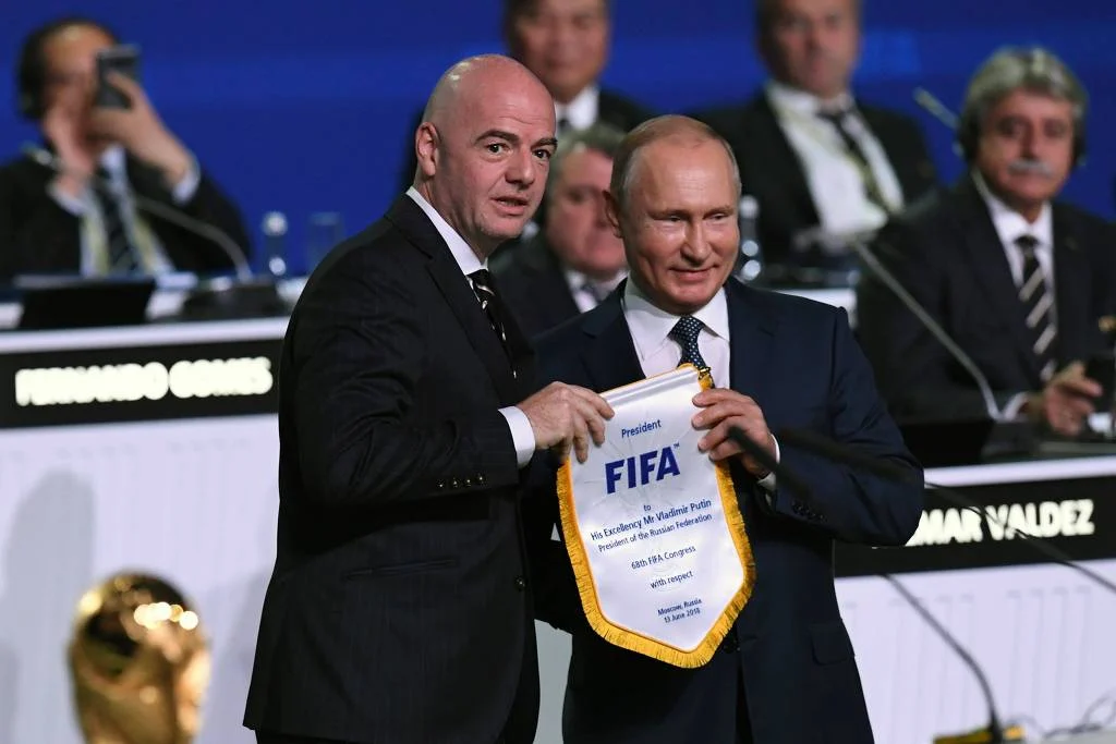 Presidente da Rússia Vladimir Putin ao lado do presidente da FIFA Gianni Infantino em Moscou em 2018, com bandeirins da entidade ao fundo