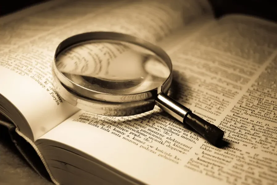 Lupa com armação metálica apoiada sobre as páginas abertas de um livro, ampliando parte do texto impresso em letras pequenas.