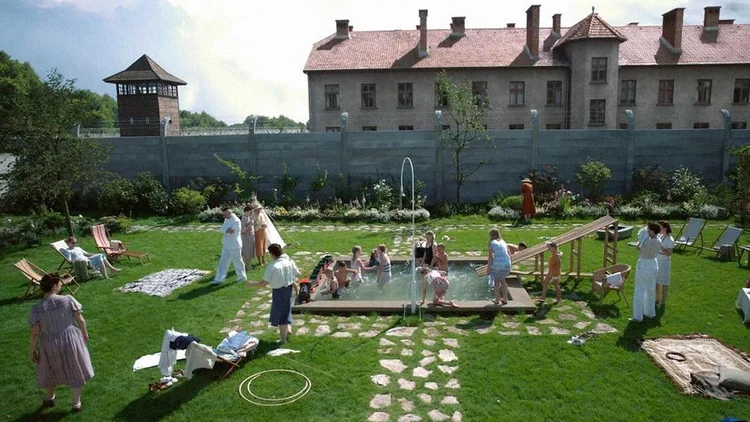 Cena do filme Zona de Interesse (2023), mostrando a família de Rudolf Höss no jardim ao lado do muro do campo de Auschwitz